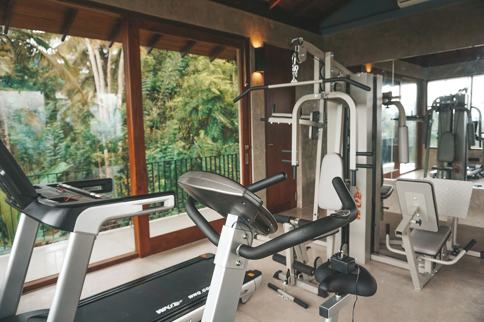 Une salle de sport équipée de machines de cardio, de poids et offrant une vue sur la verdure environnante.