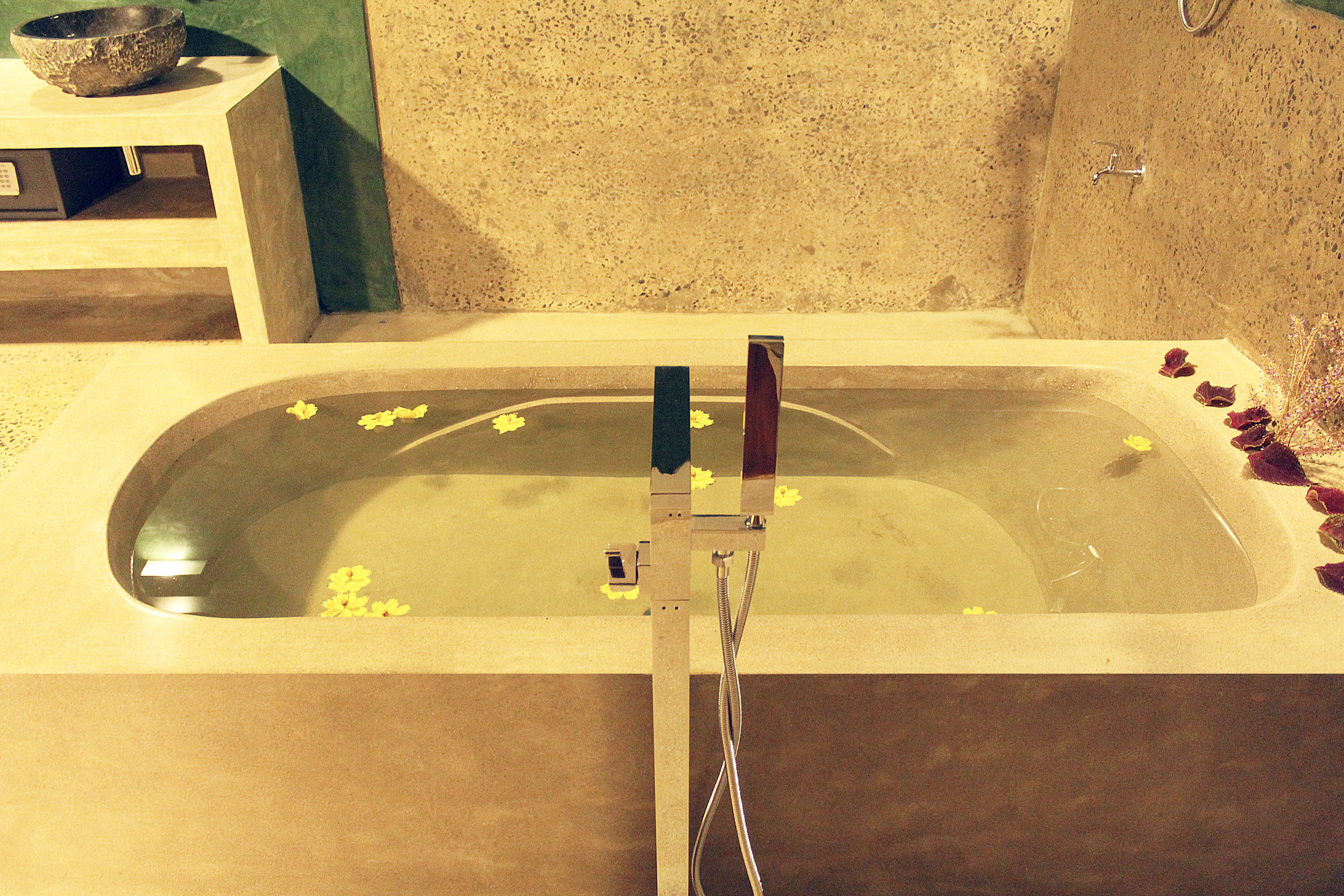 A bathtub with a showerhead, a stone basin, and a small shelf with a bowl.