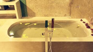 A bathtub with a showerhead, a stone basin, and a small shelf with a bowl.