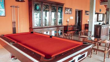 A pool table with a red felt top, wooden cabinets, and a dining area with chairs.