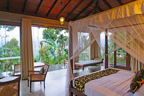 A room with a bed, a table, and chairs. There is a view of greenery outside.