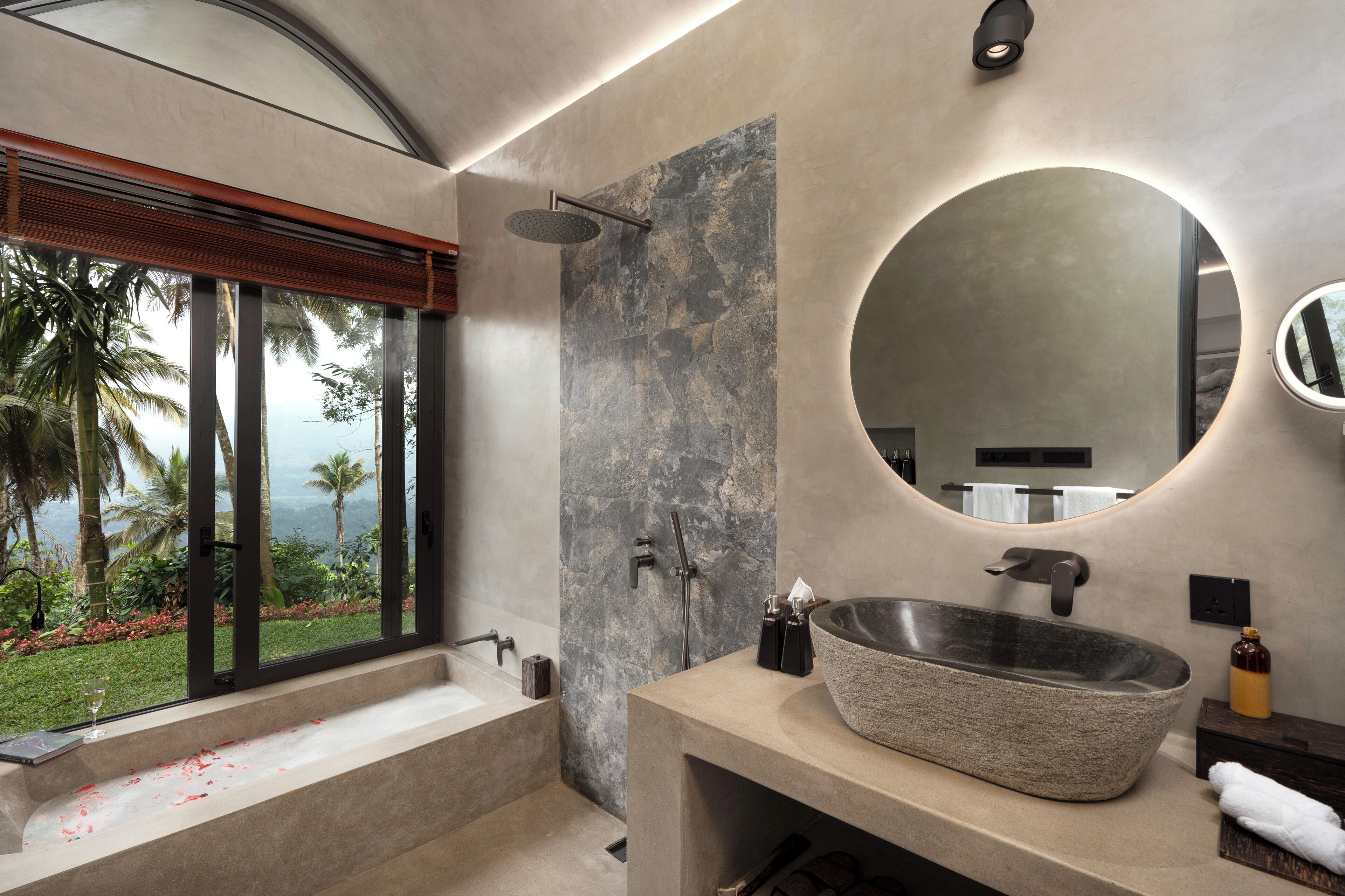 A modern bathroom with a large window, a stone sink, and a shower.