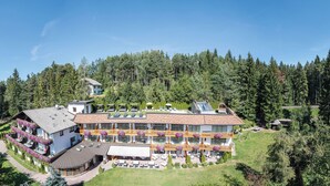 Un hotel grande de varios pisos con balcones, rodeado de un bosque denso.
