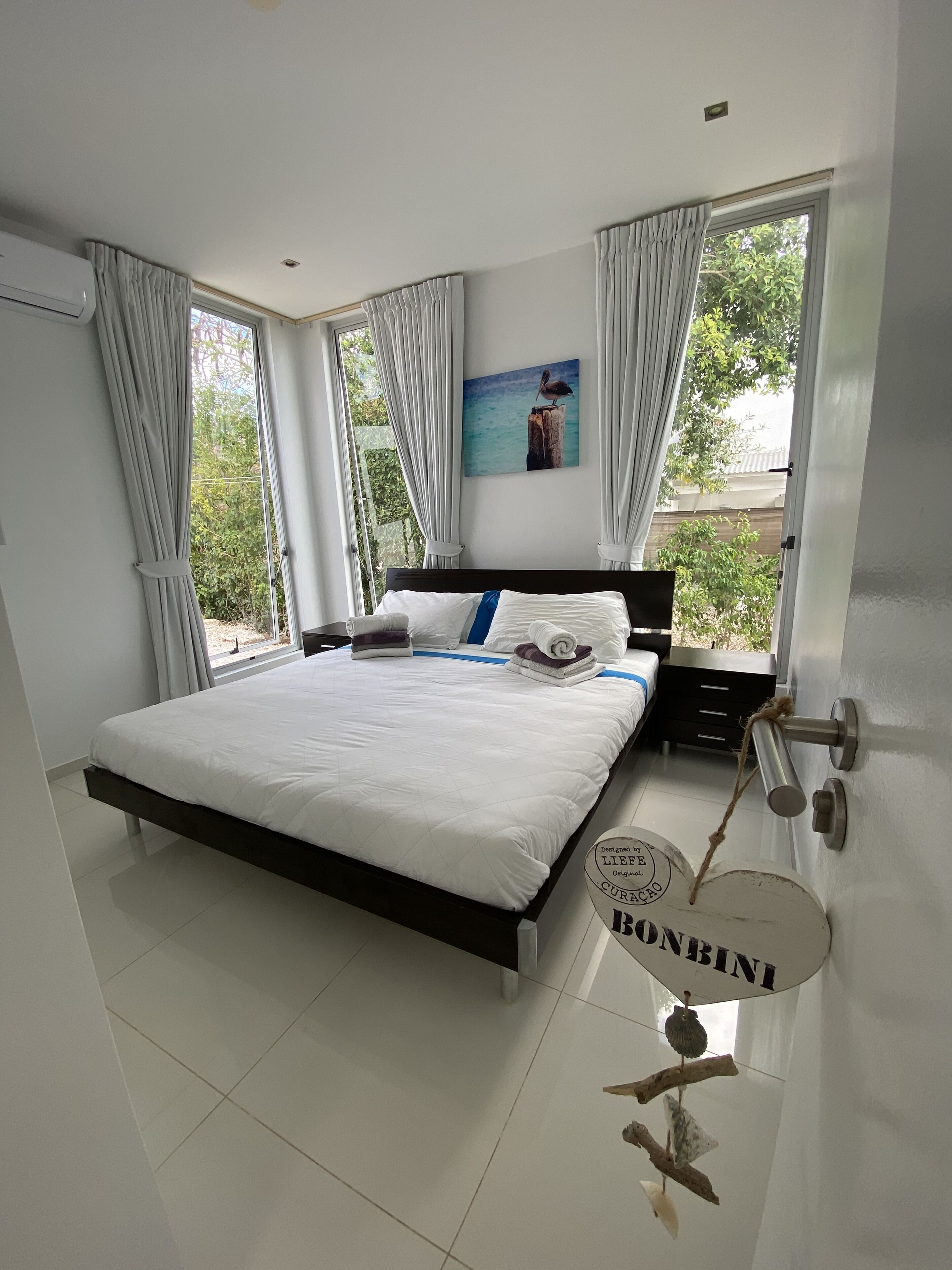 Une chambre à coucher avec un lit, des rideaux, un tableau et une vue sur la verdure.