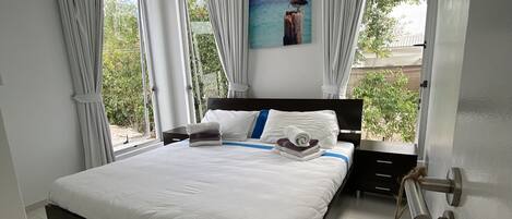 Une chambre à coucher avec un lit, des rideaux, un tableau et une vue sur la verdure.