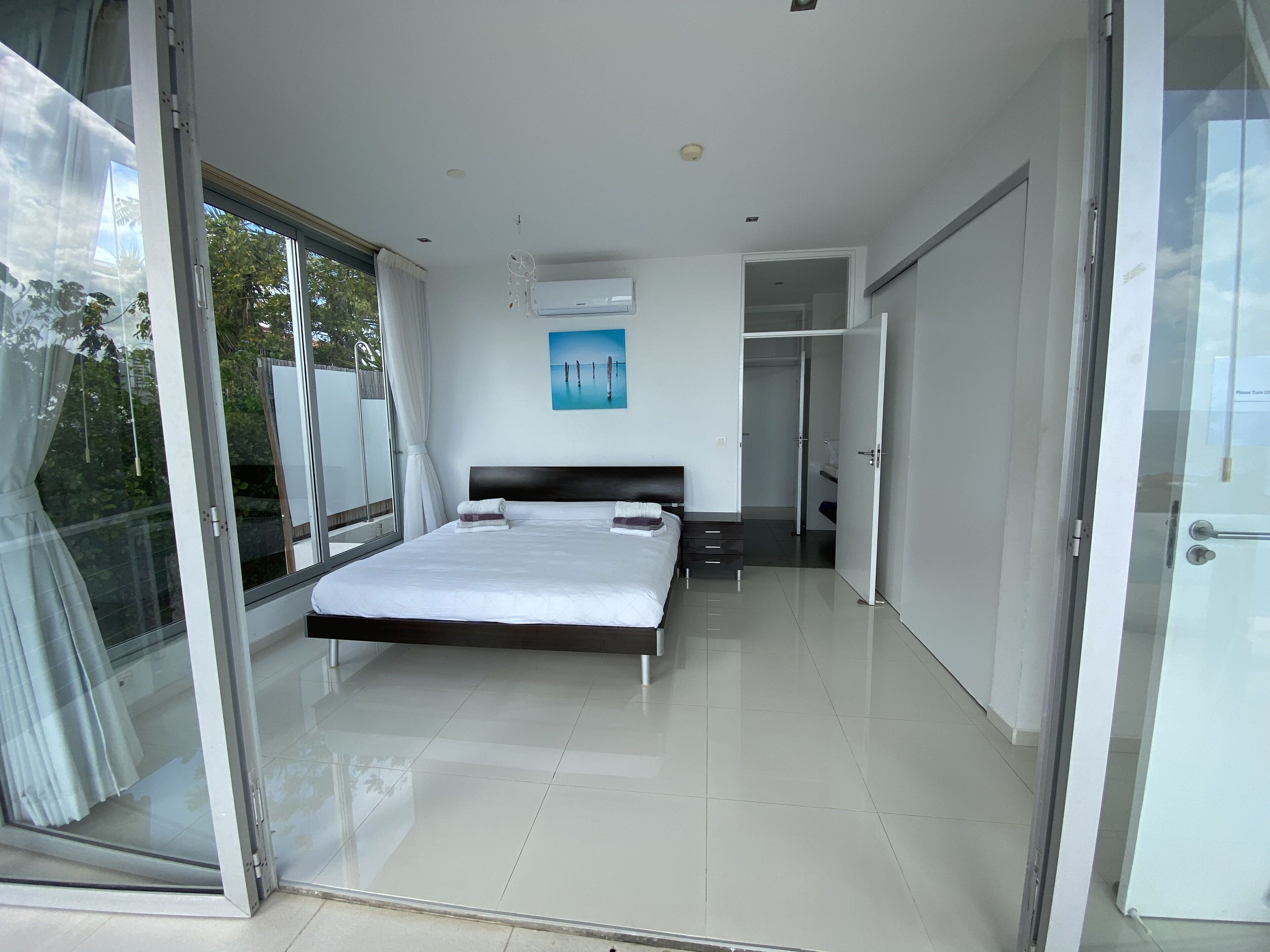 A modern bedroom with a large bed, a glass door leading to a balcony, and a view of greenery outside.