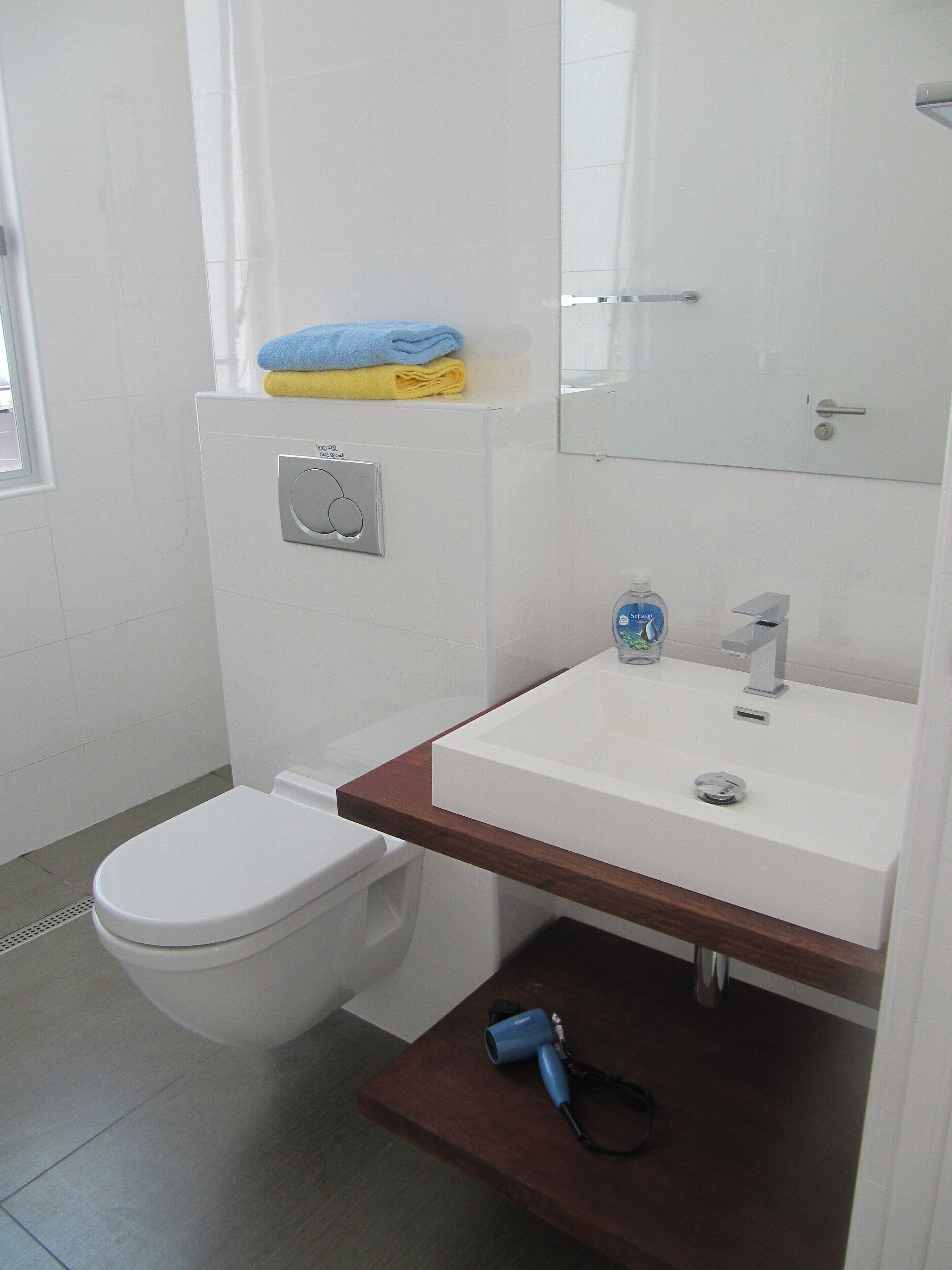 Ein modernes Badezimmer mit Toilette, Waschbecken und einem Spiegel darüber, sowie einem Handtuchhalter mit gefalteten Handtüchern.