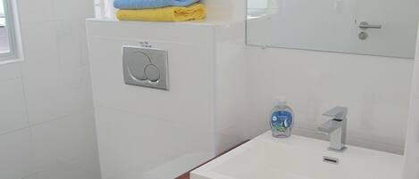 Ein modernes Badezimmer mit Toilette, Waschbecken und einem Spiegel darĂŒber, sowie einem Handtuchhalter mit gefalteten HandtĂŒchern.