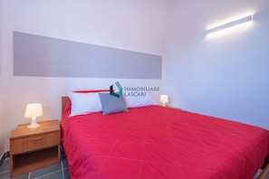 A bedroom with a red bedspread, two bedside lamps, a nightstand, and a wall-mounted light fixture.