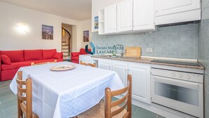 Un espace de vie compact comprenant une table à manger, un canapé rouge, une kitchenette et un escalier menant à l’étage supérieur.