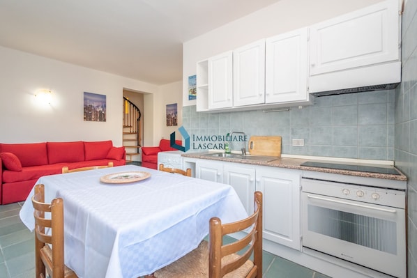 A compact living space with a dining table, red sofa, kitchenette, and a staircase leading to an upper floor.