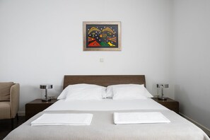 A hotel room with a bed, two bedside tables, a chair, and a framed artwork on the wall.