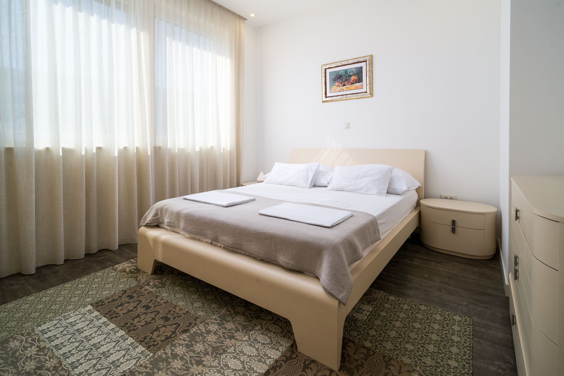 A neatly arranged hotel room with a bed, bedside tables, and a painting on the wall.