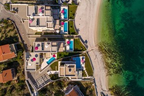 Ein Luftbild eines Küstenhotels mit mehreren Schwimmbecken, einem Strand und einer nahegelegenen Straße.