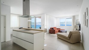 A modern living room with a kitchen area, a dining table, and a sofa. There is a large window providing a view of the sea. - Beachfront Apartment Lemonade VI (Trogir)