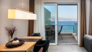 Une pièce moderne avec une table à manger en bois, un vase de fleurs et une vue sur la mer, visible à travers une porte vitrée.