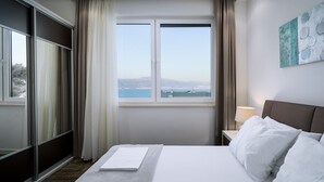 Une chambre d’hôtel avec un lit, une table de chevet, une lampe et une vue sur la mer par la fenêtre.