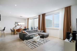 A modern living room with a sectional sofa, a glass coffee table, and a dining area with a table and chairs.