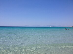 Blick auf einen Strand mit türkisblauem Wasser und entfernten Bergen.