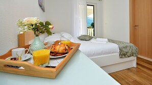 Ein Schlafzimmer mit einem Bett, einem Frühstücksbrett, einer Blumenvase und Blick ins Freie durch ein Fenster.