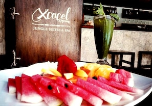 A plate of sliced watermelon and pineapple with a green drink in the background. - Xcacel Dreams Jungle Suites & Spa (Tulum)