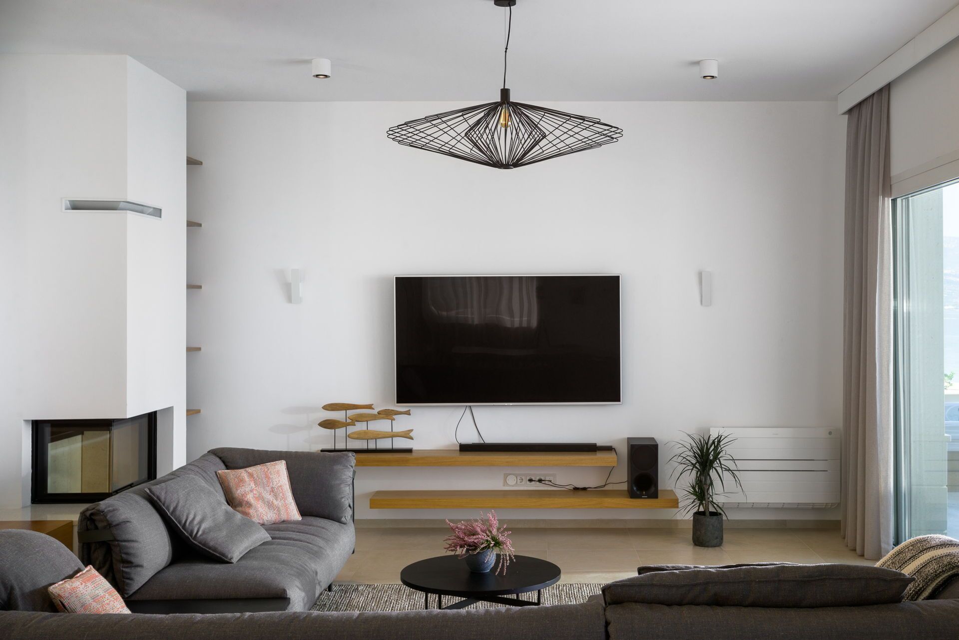 A modern living room with a large flat-screen TV, a geometric pendant light, and a minimalist design.