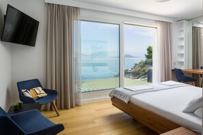 Quarto de hotel com cama, escrivaninha, cadeira, televisão e vista para o mar.