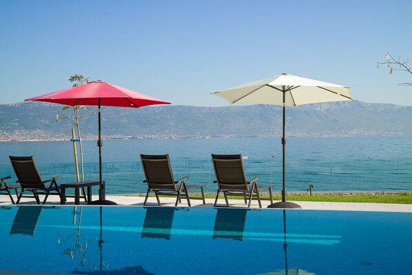 A poolside area with lounge chairs and umbrellas, overlooking a body of water and mountains.