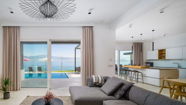 Un salon moderne avec un canapé gris, une table basse ronde et une vue sur une piscine et des montagnes.