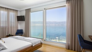 Une chambre d’hôtel avec un grand lit, une chaise, une télévision et une vue sur la mer.