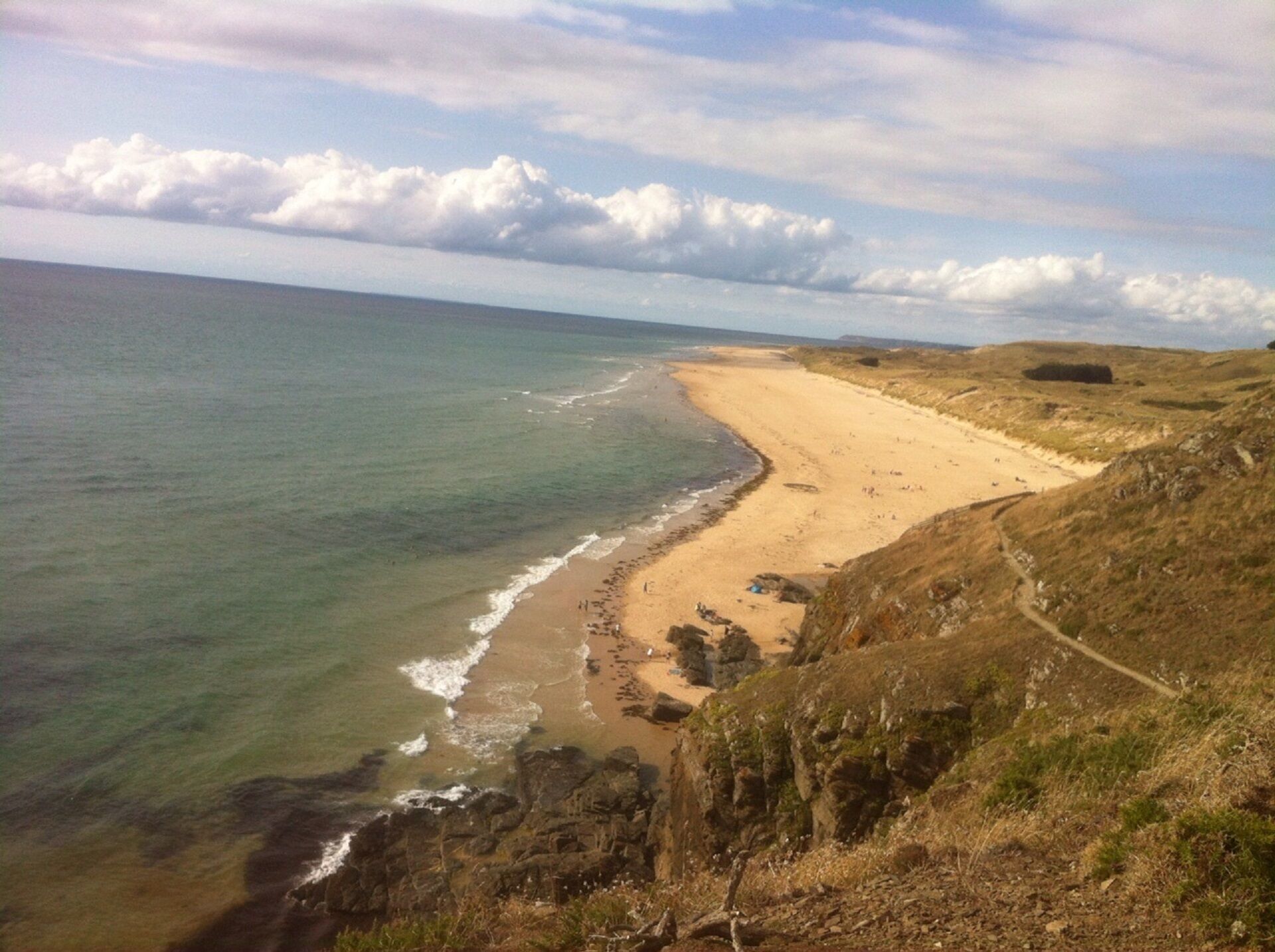 Eine Küstenlandschaft mit Sandstrand, Felsen und freiem Blick auf den Ozean.