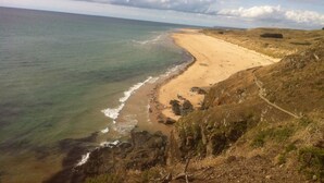A coastal landscape with a sandy beach, rocky cliffs, and a clear view of the ocean.