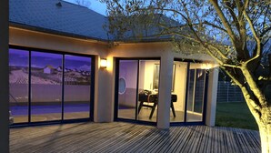 A modern house with large glass doors leading to a covered outdoor area with a pool.