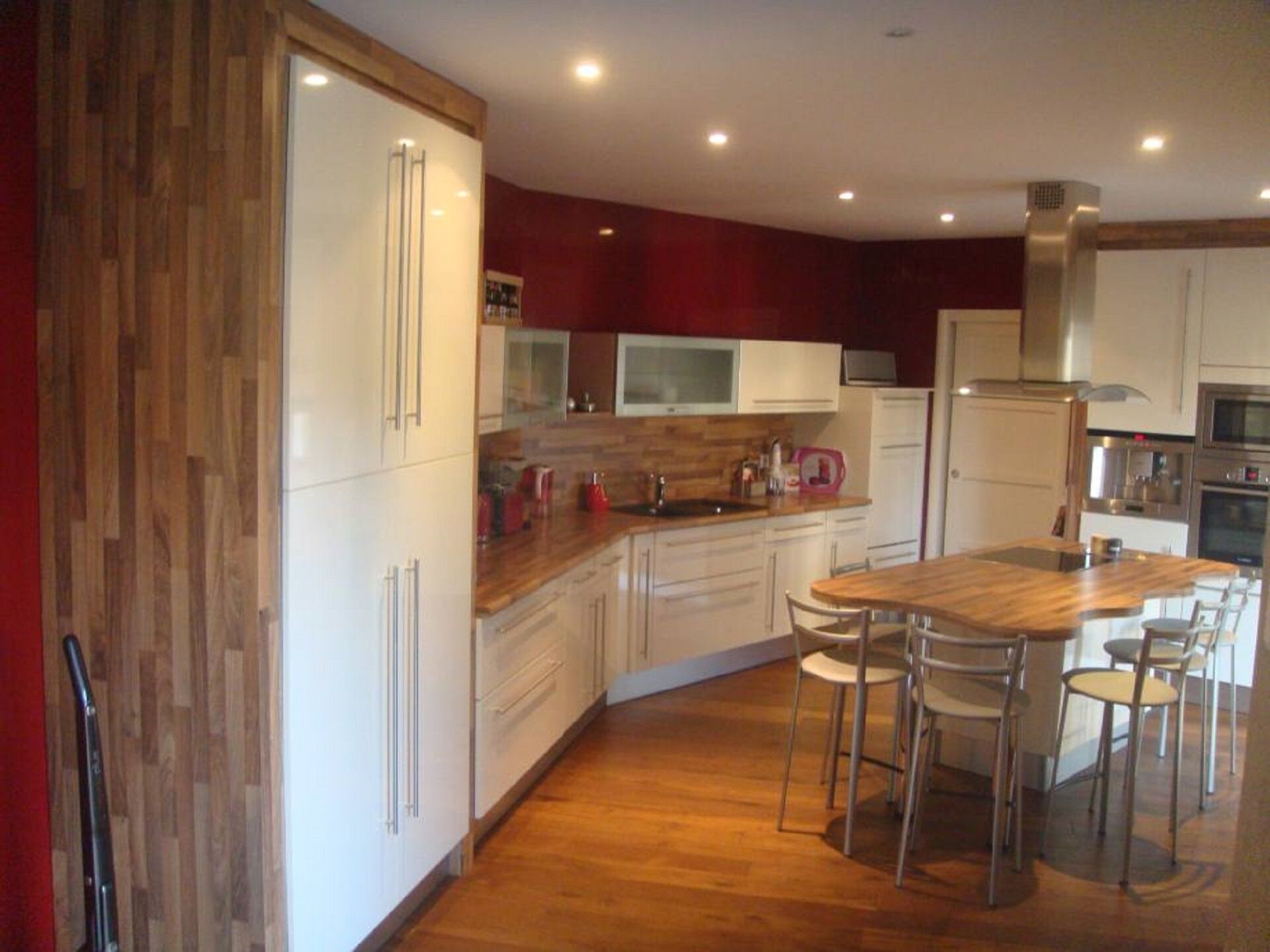 A modern kitchen with white cabinets, a wooden countertop, and a central island with chairs.