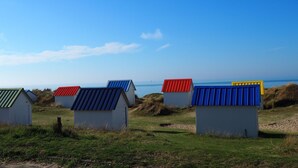A row of beach huts with corrugated metal roofs, set against a clear blue sky and the sea in the background.