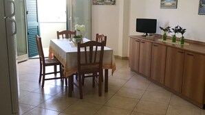 A dining area with a table and chairs, a kitchen counter with a TV, and a painting on the wall. - Apartment On the Beaches of Gallipoli (Gallipoli)