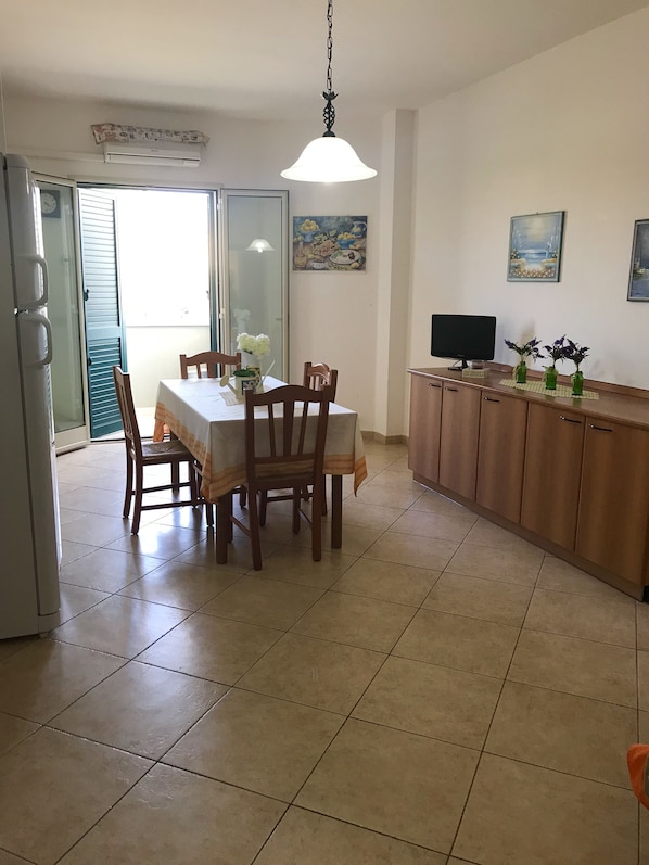 A dining area with a table and chairs, a kitchen counter with a TV, and a painting on the wall.