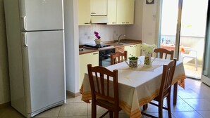 A kitchen with a refrigerator, stove, sink, and wooden chairs around a table with a white tablecloth. - Apartment On the Beaches of Gallipoli (Gallipoli)