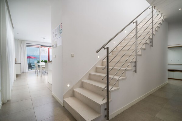 A modern interior with a staircase, a dining area with a table and chairs, and a view through a glass door. - Beachfront Apartment Lemonade with Pool I (Trogir)