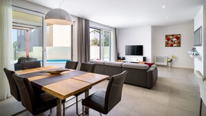 Ein modernes Wohnzimmer mit Essbereich, einer Couch, einem Fernseher und Blick ins Freie.