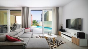 Ein modernes Wohnzimmer mit einer großen Couch, einem Flachbildfernseher und Blick auf einen Pool.