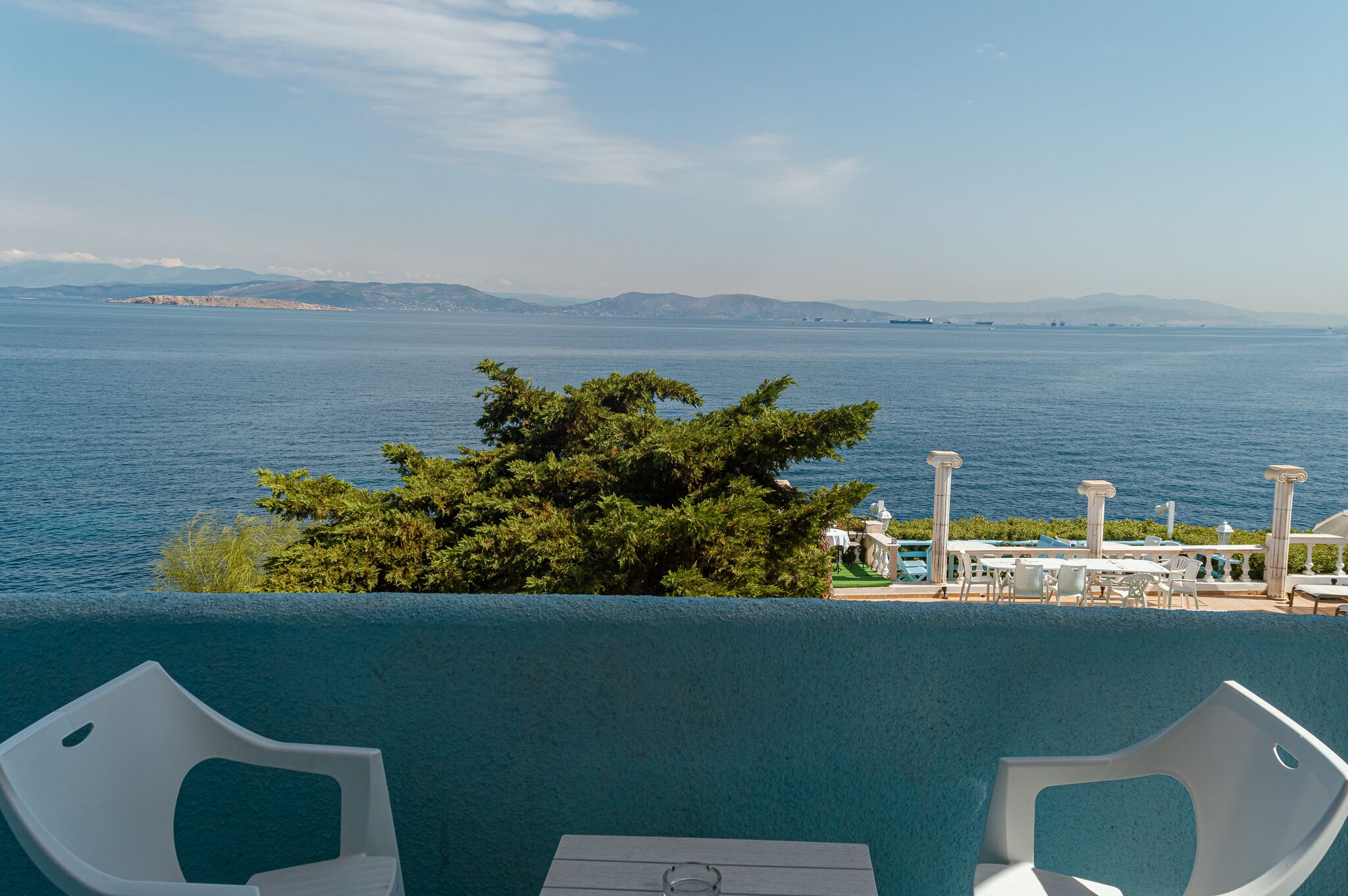 A balcony with a view of the sea, a tree, and outdoor seating.