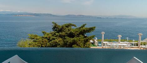 A balcony with a view of the sea, a tree, and outdoor seating.