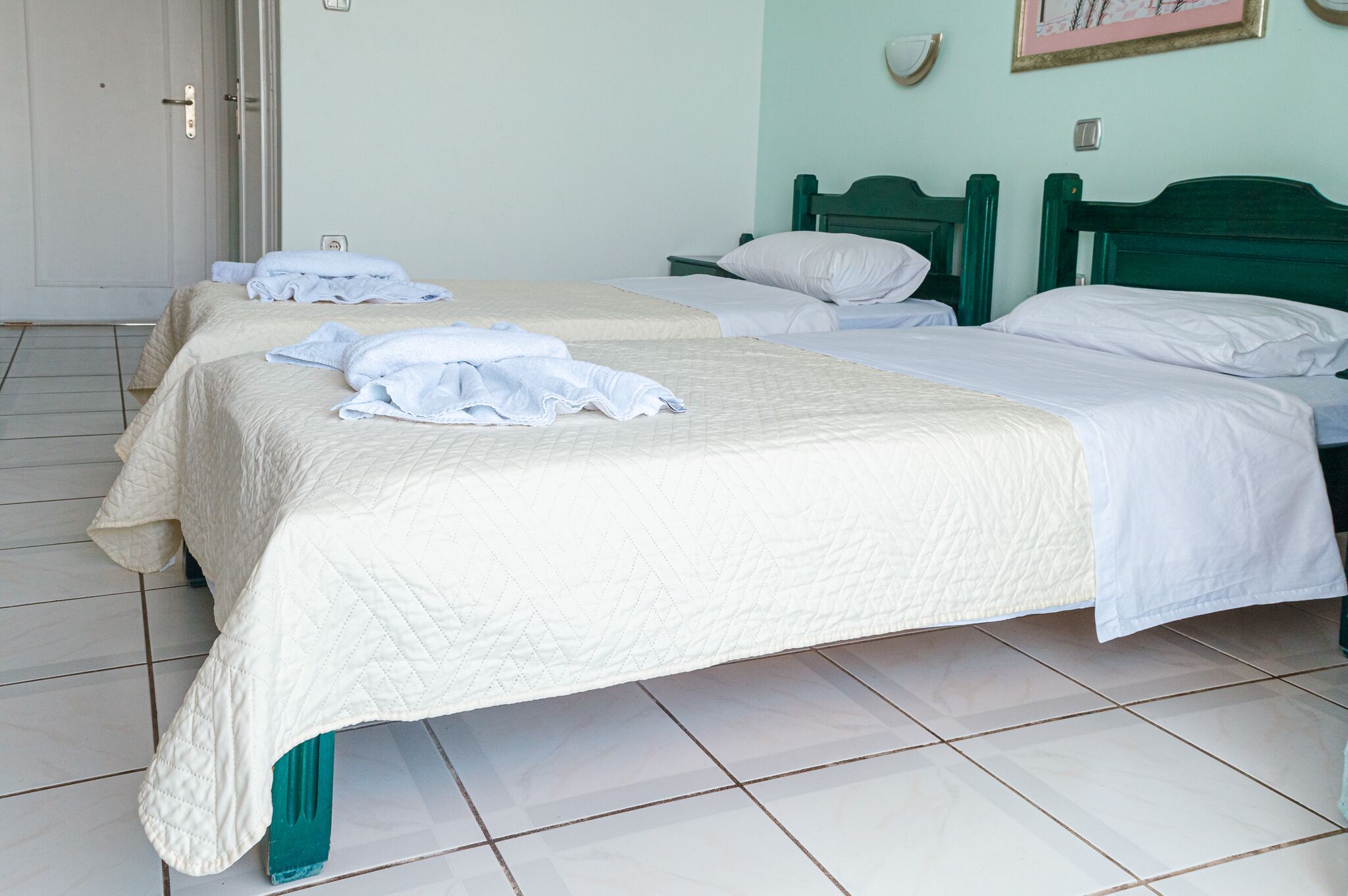 A hotel room with two beds, each with a quilted bedspread and pillows.
