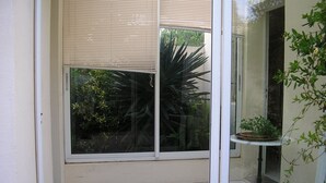 A room with a large window, a potted plant on a small table, and a tiled floor.