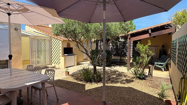 A patio area with a table and chairs, a grill, and a pergola with an umbrella.