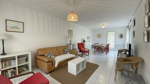 A living room with a brown sofa, a red chair, a dining table with chairs, a white coffee table, and a bookshelf.