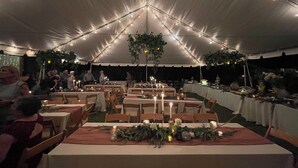Un área de comedor al aire libre con carpas, mesas dispuestas para comensales, luces colgantes y plantas suspendidas.