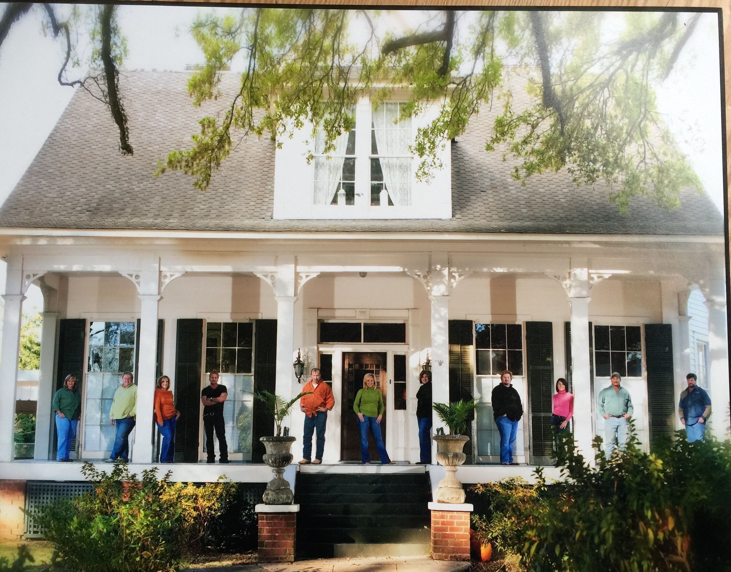 A two-story house with a porch, columns, and a large window.
