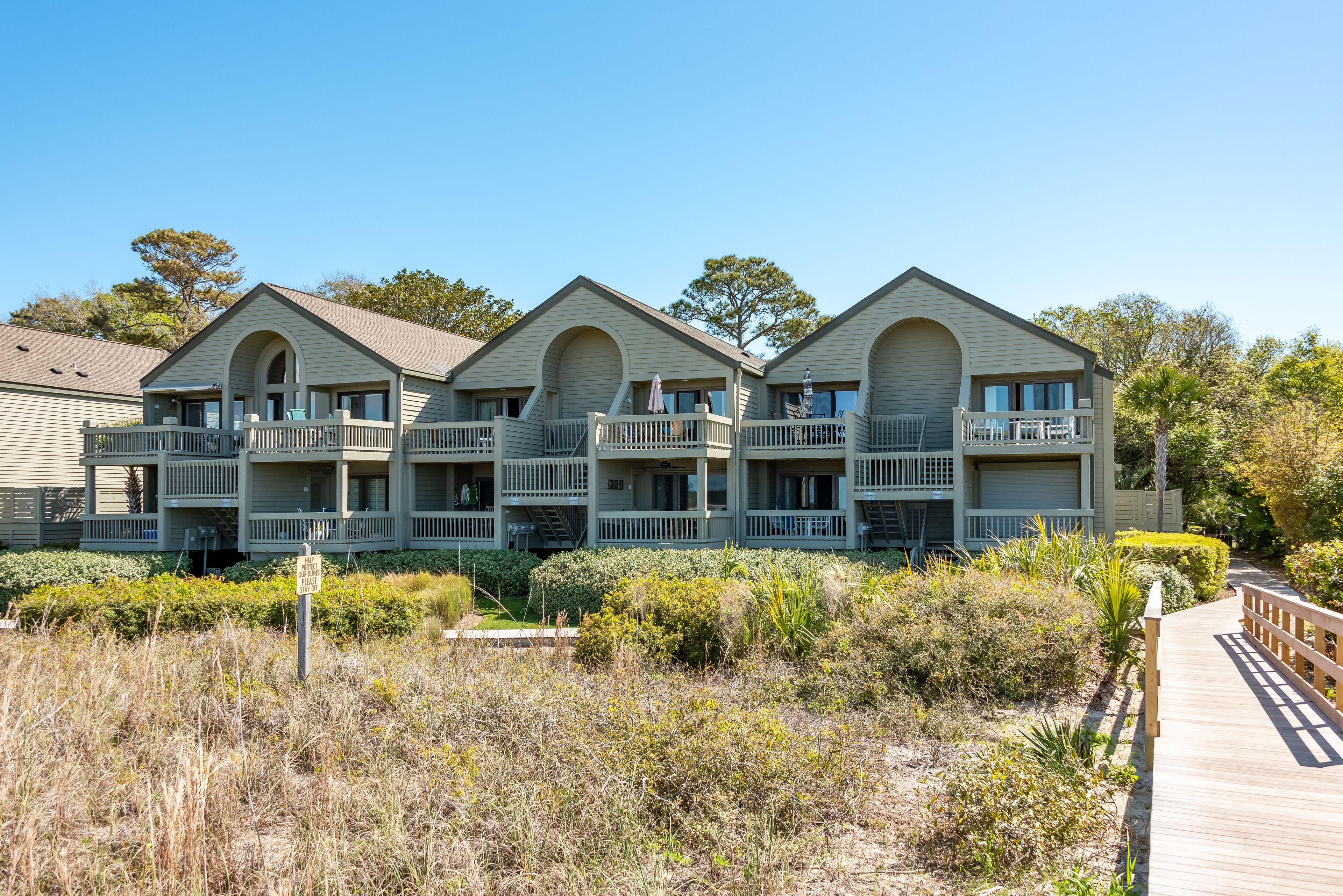 A beachfront hotel with multiple balconies, a wooden boardwalk, and a clear view of the ocean.